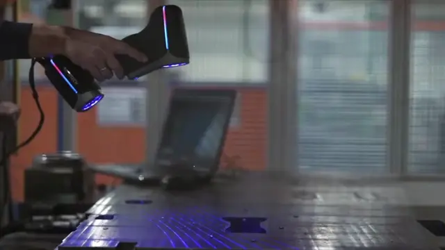 Ręczny skaner 3D nad metalową płytą — kadr z filmu o inżynierii wstecznej