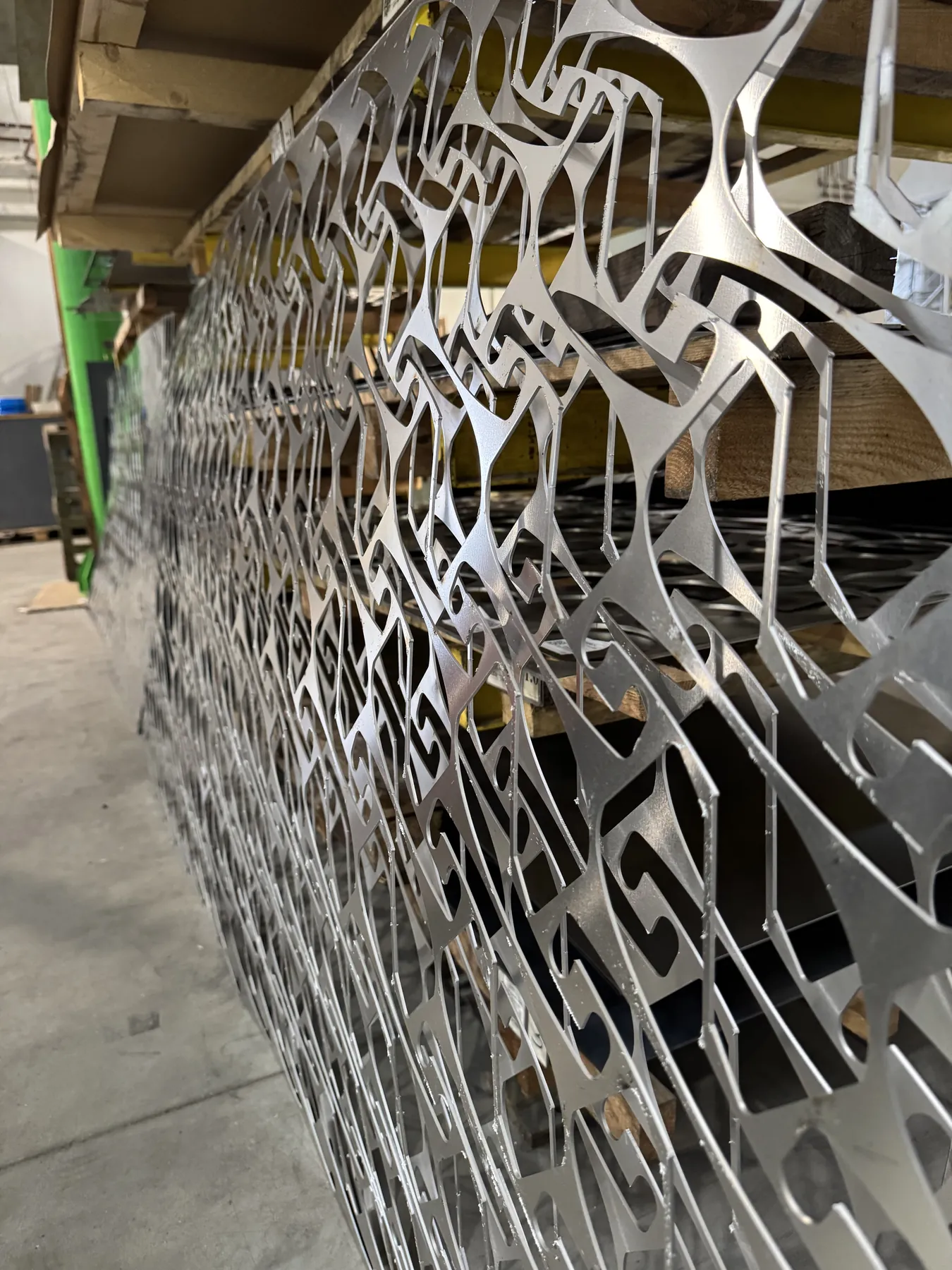 Panneau ajouré en tôle fine au motif découpé dense, appuyé contre un rayonnage à palettes.