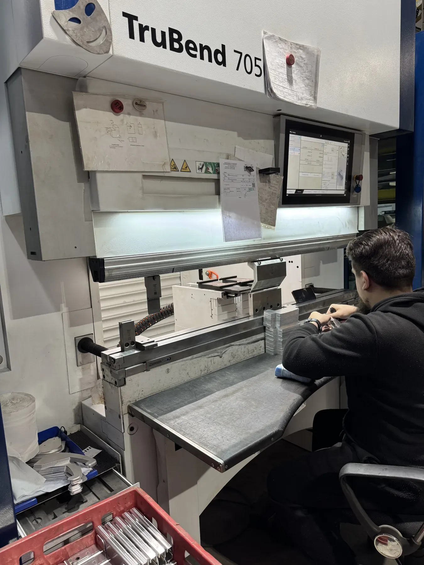 Opérateur devant la presse plieuse Trumpf TruBend 7050 avec écran de commande, à côté d'un bac de pièces.