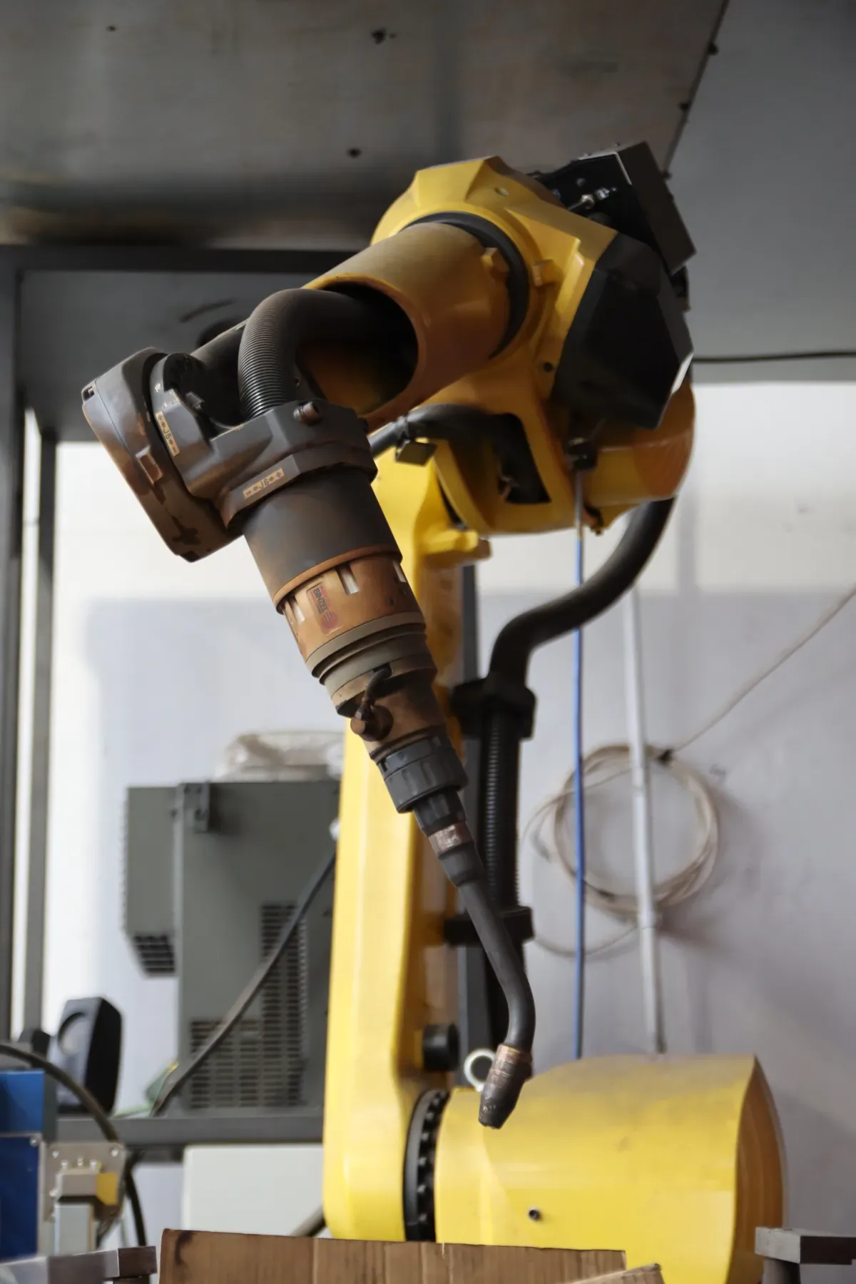 Bras jaune d'un robot de soudage avec torche et faisceau, en gros plan.