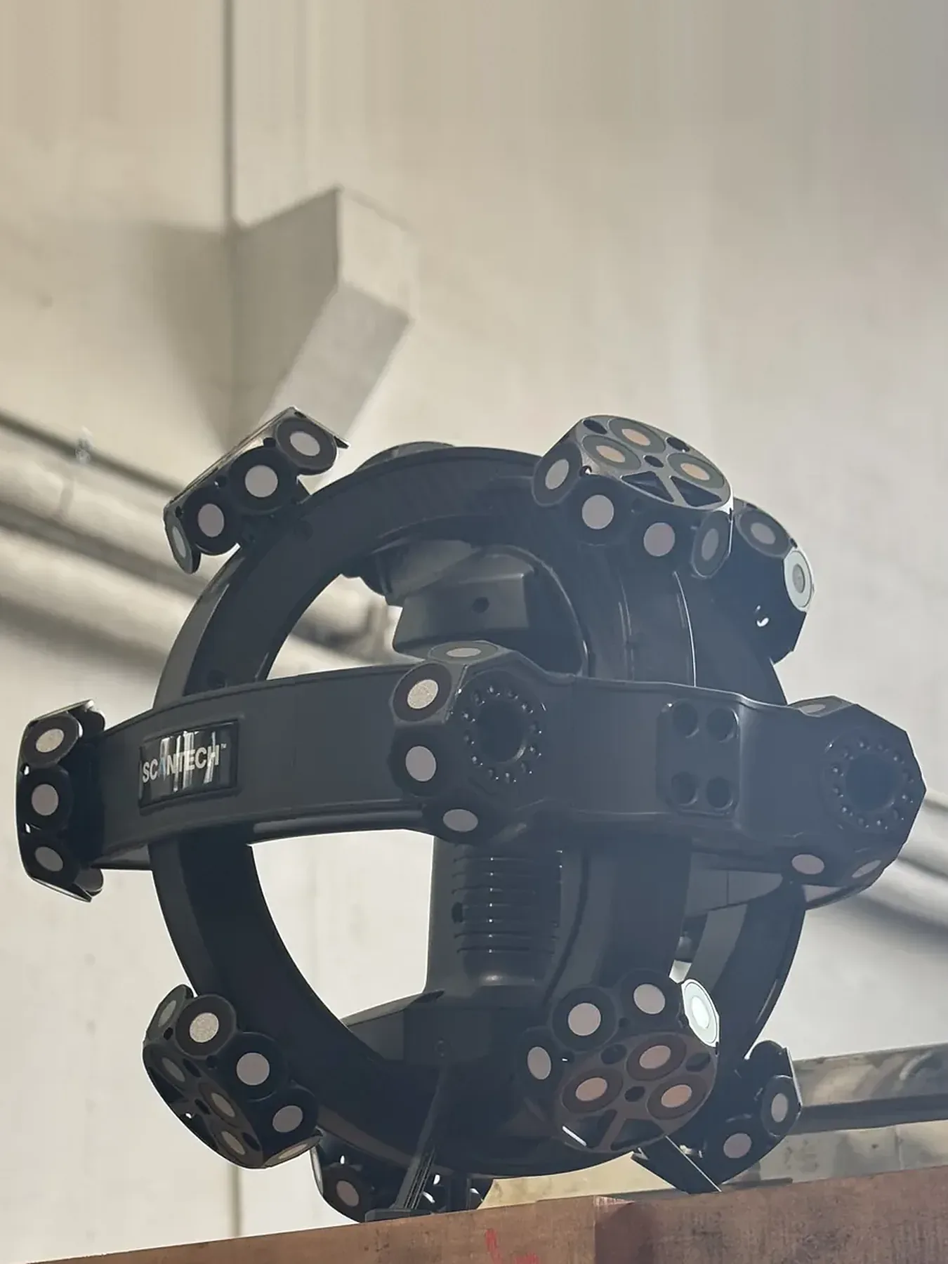 Scanner 3D portable Scantech NimbleTrack : corps noir en forme d'anneau avec cibles rondes, posé sur une table dans l'atelier.