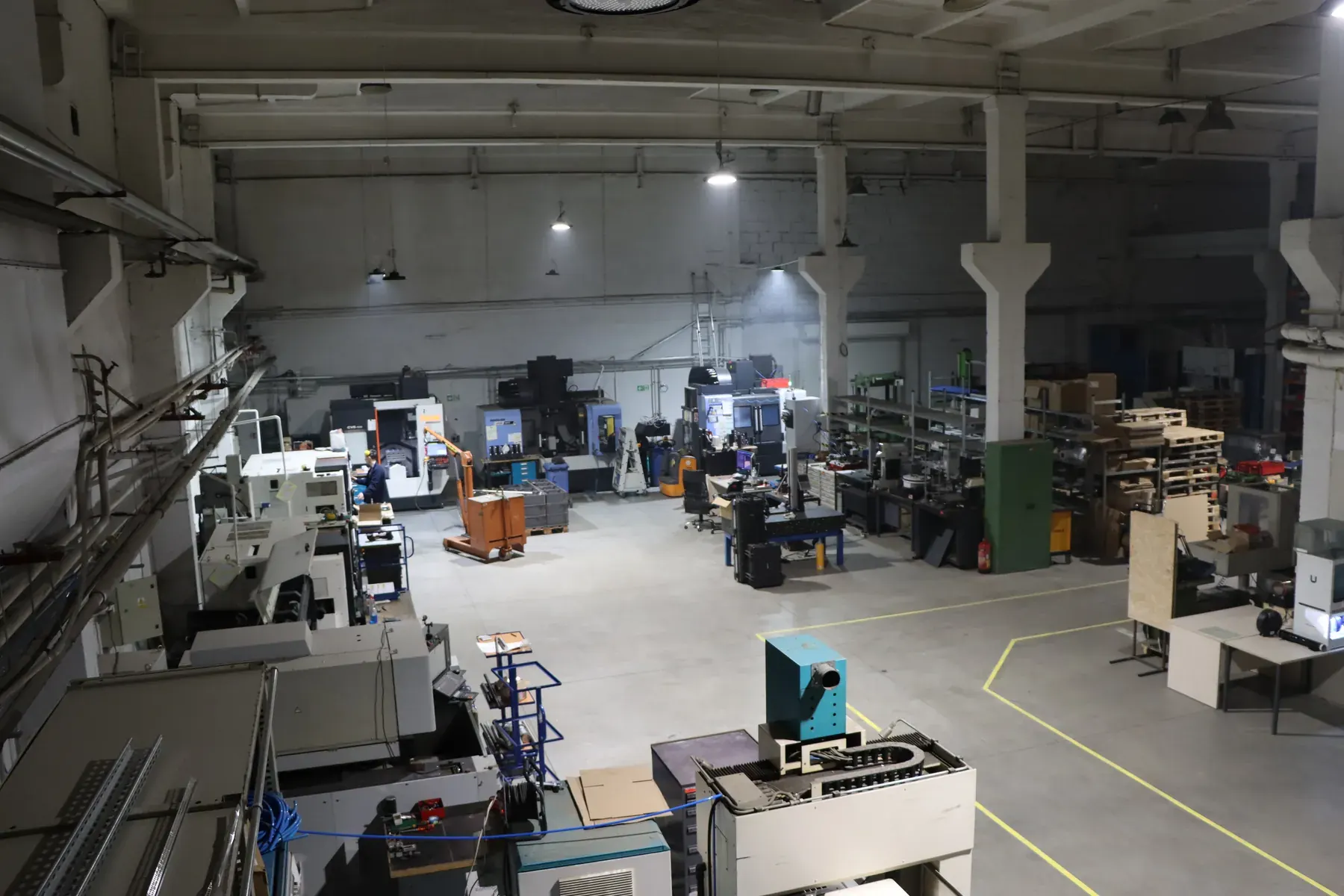Atelier de production vu de dessus : rangées de tours et centres d'usinage CNC, postes informatiques, chariots et racks à matière.