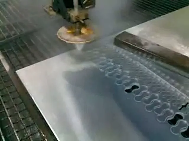 Découpe au jet d'eau d'aluminium : tête de découpe au-dessus de la tôle, rangées de contours de pièces en forme de huit sur la tôle, brouillard d'eau autour.