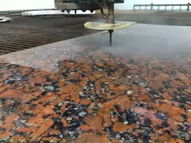 Découpe au jet d'eau de granit : buse de la machine de découpe au-dessus d'une dalle de granit rouge sur une table à caillebotis.