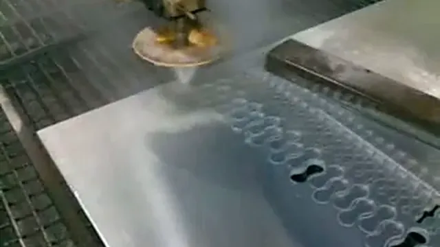 Tête de découpe au jet d'eau au-dessus d'une tôle d'aluminium avec pièces découpées, extrait d'une vidéo de 2009.