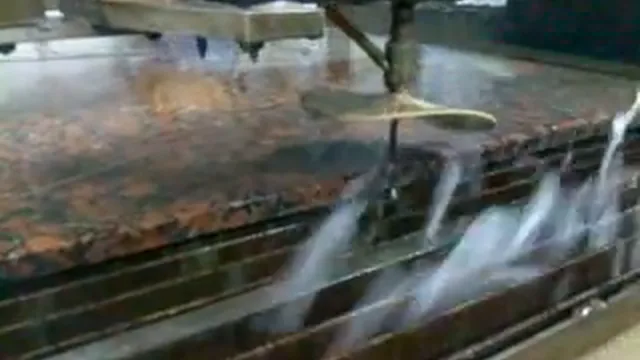 Tête de découpe au jet d'eau au-dessus d'une dalle de granit humide, extrait d'une vidéo de 2009.