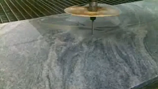 Découpe de granit au jet d'eau : buse au-dessus d'une dalle de granit gris, extrait d'une vidéo de 2009.