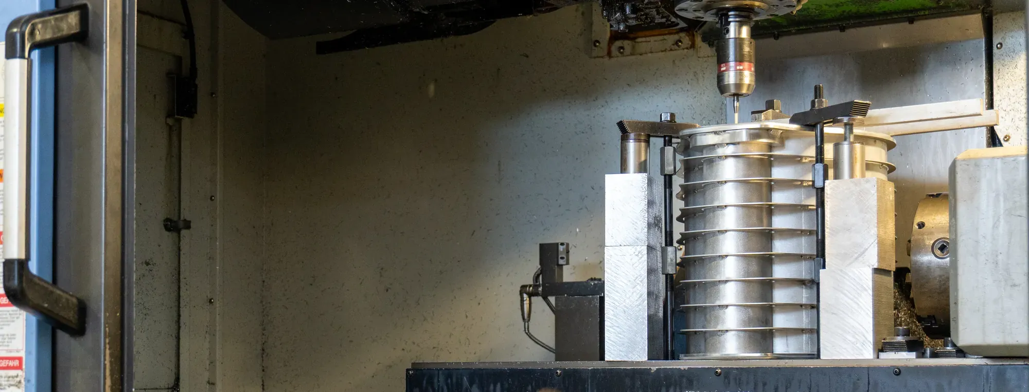 Enceinte d'un centre d'usinage portes ouvertes : pièce en aluminium nervurée bridée sur la table, surmontée d'une broche avec palpeur.